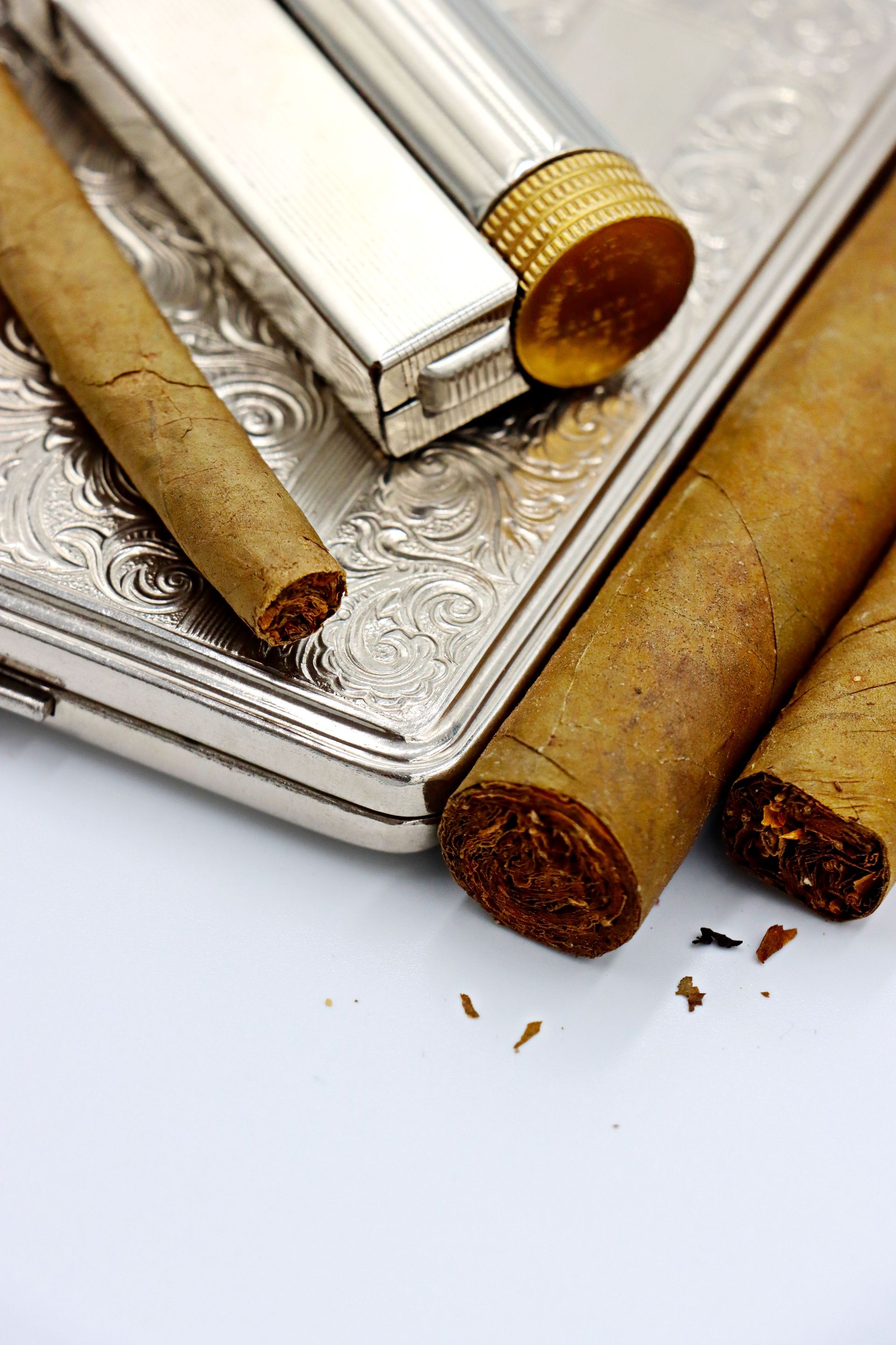 Close-up of cigars and a silver lighter on a white background, showcasing luxury and craftsmanship.